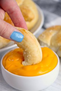 a person dipping something into a bowl with orange sauce on it and bread rolls in the background