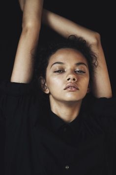 a woman with her hands on her head and eyes closed, wearing a black shirt