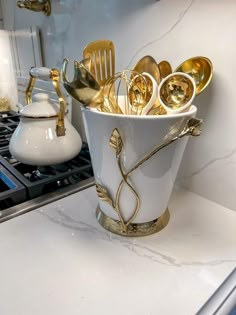 a white vase filled with gold spoons on top of a counter next to a stove