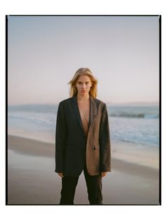 a woman standing on top of a sandy beach next to the ocean in a suit