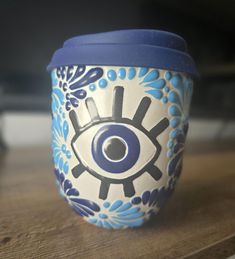 a blue and white cup with an evil eye on the lid sitting on a table