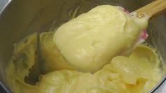 a wooden spoon in a metal bowl filled with yellow batter and butter, on top of a stove