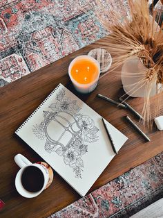 a table with a coffee cup, pen and notebook on it next to a vase