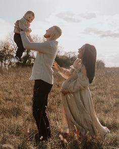 a man holding a baby up in the air while standing next to a woman and child