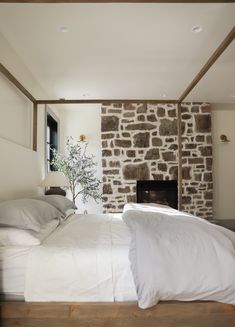 a bed with white sheets and pillows in front of a stone fireplace