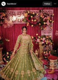 a woman in a green lehenga posing for the camera with flowers behind her