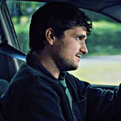 a man sitting in the driver's seat of a car with his hand on the steering wheel