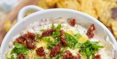 a white bowl filled with food sitting on top of a wooden table next to chips