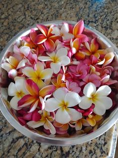 a bowl filled with pink and white flowers on top of a marble countertop next to a knife