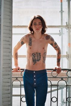 a shirtless man with tattoos on his chest and arms standing in front of a railing