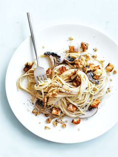 a white plate topped with pasta covered in sauce and toppings next to a fork