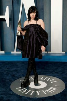 a woman in black dress holding an award at the oscars awards ceremony on blue carpet