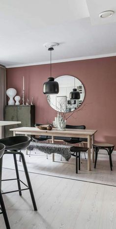 a dining room with pink walls and black chairs in front of a wooden table, round mirror on the wall