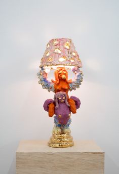 a colorful lamp sitting on top of a wooden block in front of a white wall