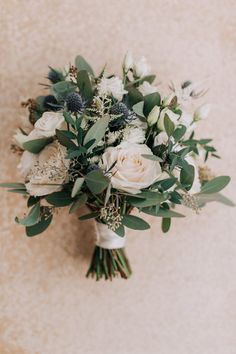 a bridal bouquet with white flowers and greenery on the wall in front of it