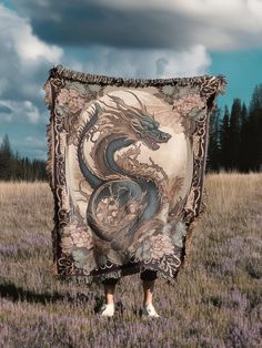 a woman standing in a field holding up a blanket with an image of a dragon on it