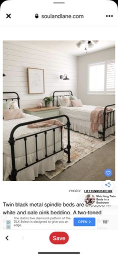 two beds in a room with white walls and black metal frames, one bed has pink pillows on it