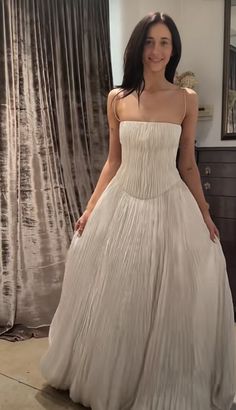 a woman standing in front of a mirror wearing a white dress and smiling at the camera