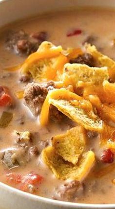 a close up of a bowl of soup with cheese and other foods in it on a table