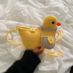 a crocheted yellow ducky bag and purse on a white sheet with a hand holding it