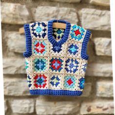 a blue and white crocheted sweater hanging on a clothes line next to a brick wall