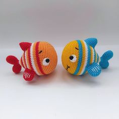 two knitted toy fish sitting next to each other on a white surface with one looking at the camera