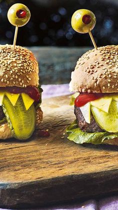 two hamburgers with pickles and cheese on them sitting on a wooden cutting board