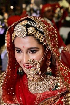 a woman wearing a red and gold bridal outfit with jewelry on her face is smiling at the camera