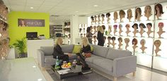 two women sitting on couches in front of a wall full of wigs