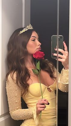 a woman in a yellow dress holding a rose and taking a selfie with her cell phone