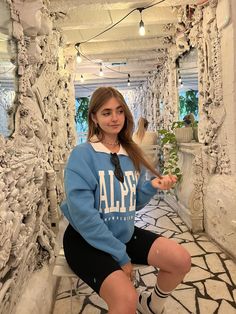 a woman sitting on the ground with her legs crossed and wearing a blue sweatshirt that says alpy