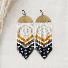 two pairs of beaded earrings on a white cloth with black, yellow and brown beads