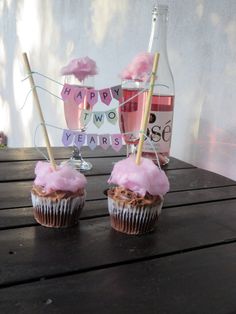 two cupcakes with pink frosting and decorations on them sitting on a table