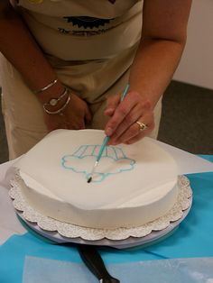 a woman is cutting into a cake with blue writing on the frosting and white icing