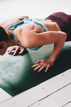 a woman in a sports bra top is doing push ups on a yoga mat with her hands behind her head