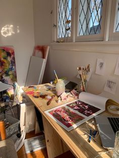 an artist's desk with art supplies and watercolors in front of the window