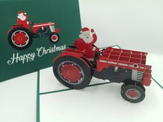 a christmas card with a tractor and santa clause on the front, sitting next to a greeting card