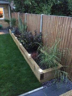 a wooden planter filled with lots of plants next to a fenced in yard