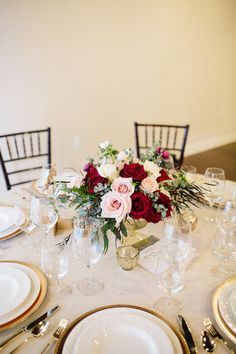 a white table topped with plates and vases filled with red and pink flowers on top of it