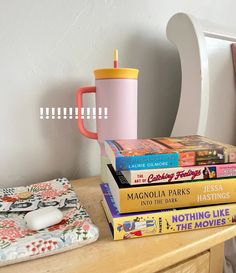 a stack of books sitting on top of a wooden table next to a pink coffee mug