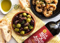 a bowl of olives, bread and wine are sitting on a yellow striped towel