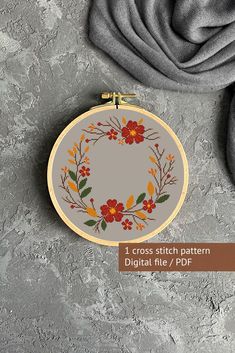 a cross stitch pattern with flowers and leaves in the center on a gray surface next to a grey scarf