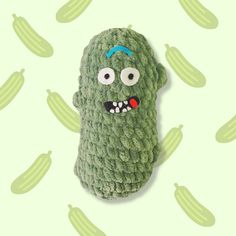 a crocheted green object with eyes and mouth on a white surface surrounded by cacti