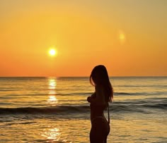 a woman standing on top of a sandy beach next to the ocean at sunset or dawn