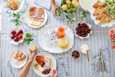 people are sitting at a table with plates and food on it, including bread, fruit, cheese, crackers, and wine glasses