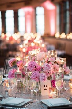 the table is set with candles and pink flowers in vases on each place setting