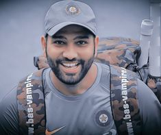 a man with a baseball cap and uniform holding a bat in one hand and smiling at the camera