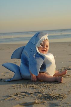 a baby in a shark costume sitting on the beach