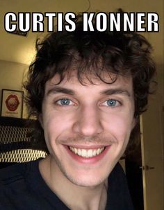 a man with curly hair and blue eyes smiles at the camera while wearing a black shirt