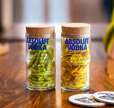 two glass jars filled with pickles sitting on top of a wooden table next to one another